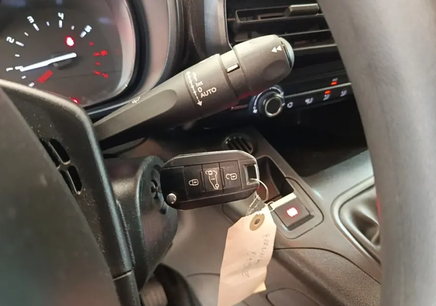 Gros plan intérieur sur le volant et le tableau de bord du Citroën Berlingo blanc avec clé insérée et commandes visibles.