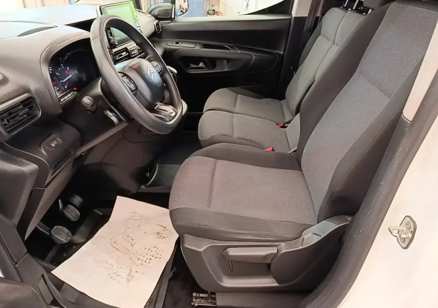 Vue intérieure côté conducteur du Citroën Berlingo blanc 2021, montrant le volant multifonctions et les sièges gris.
