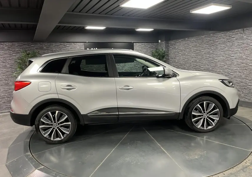 Profil côté gauche d'un Renault Kadjar gris platine 2017 avec jantes alliage 19 pouces dans un showroom.