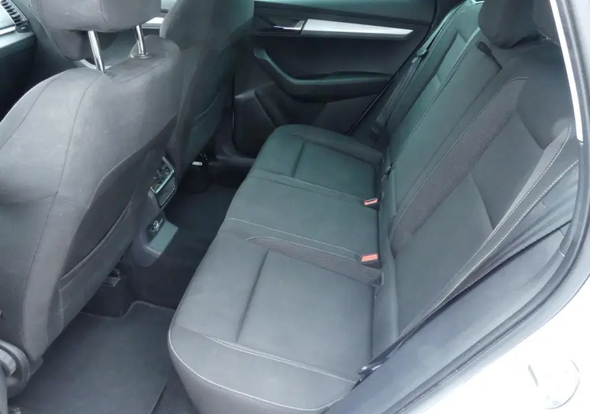 Vue intérieure côté droit de la banquette arrière noire tissu du Skoda Karoq blanc 2024 avec appuie-têtes et aérateurs centraux.