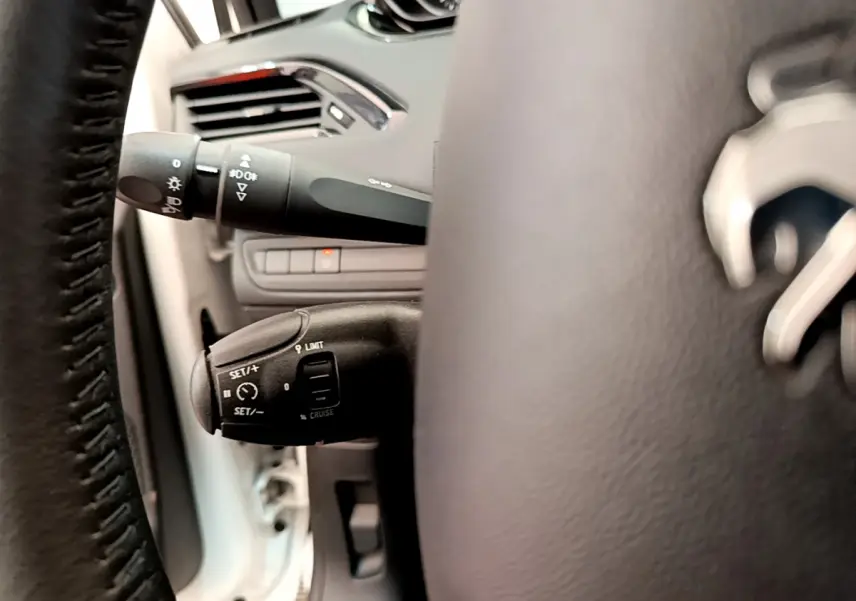 Gros plan sur le volant cuir et les commandes de régulateur de vitesse à gauche dans l’habitacle d’une Peugeot 208 blanche.