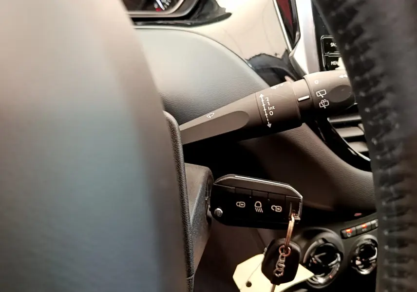 Gros plan sur la clé insérée et la commande d'essuie-glace du tableau de bord d'une Peugeot 208 Puretech 82 Signature.
