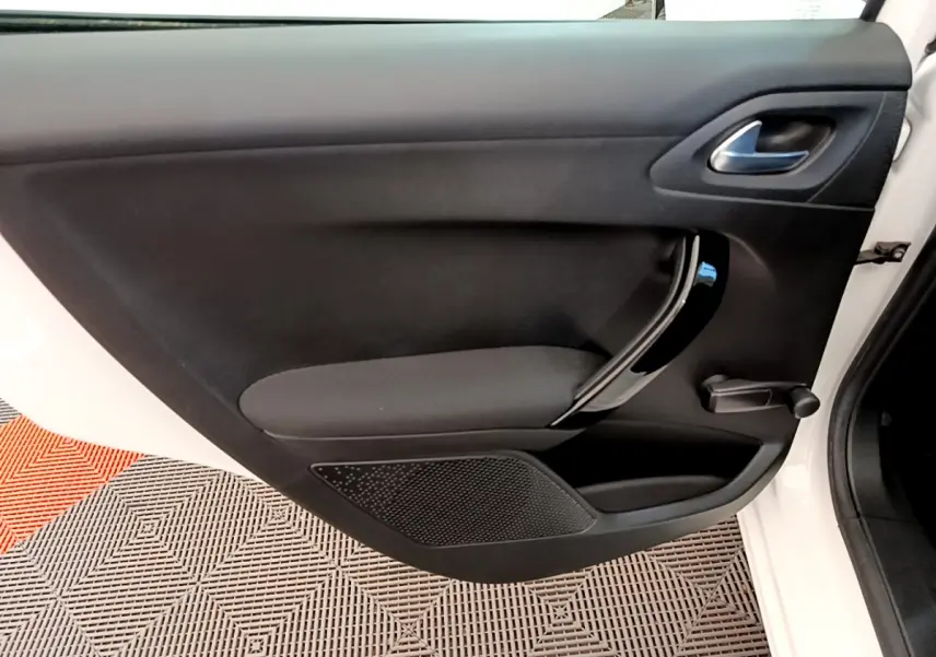 Porte intérieure côté gauche de la Peugeot 208 blanche, avec poignée noire brillante et manivelle de vitre manuelle.
