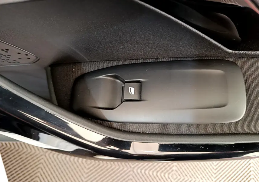 Gros plan sur le bouton de lève-vitre côté conducteur d'une Peugeot 208 blanche, intérieur noir.