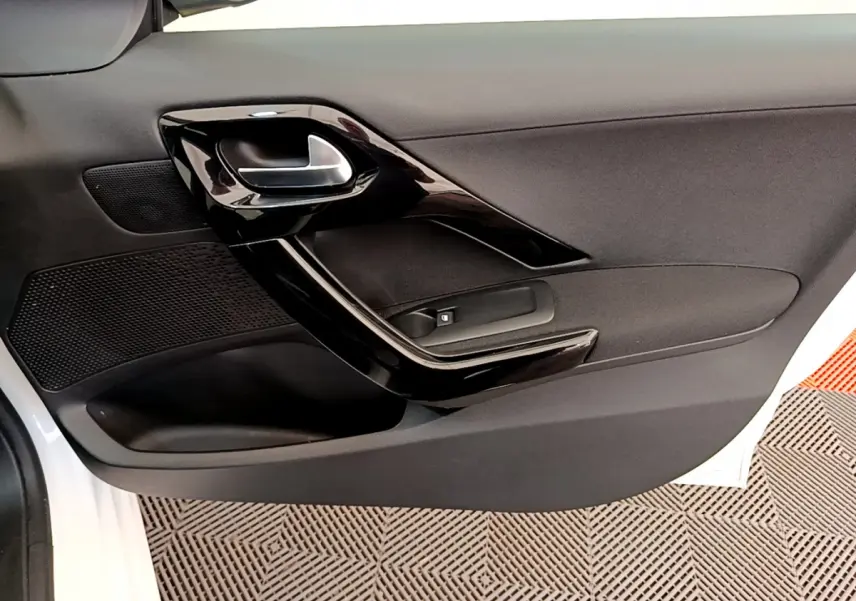 Gros plan sur la porte côté gauche de la Peugeot 208 blanche, montrant la poignée intérieure noire brillante et le bouton de lève-vitre.