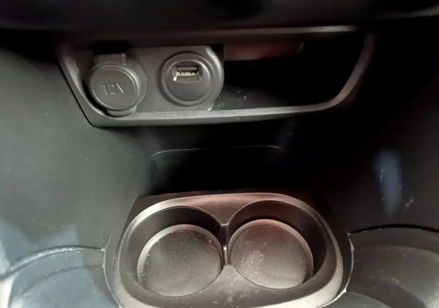 Gros plan sur la prise 12V et port USB au-dessus des porte-gobelets dans l’habitacle noir de la Peugeot 208 blanche