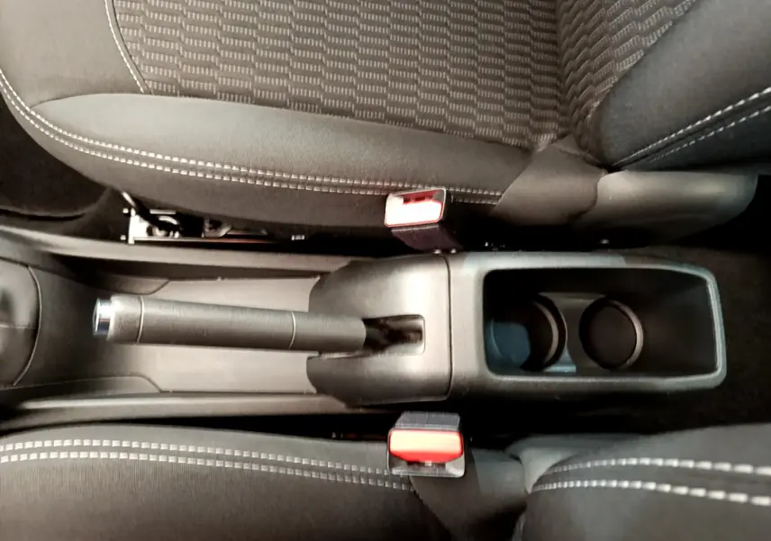 Vue plongeante sur le frein à main manuel et porte-gobelets entre les sièges noirs à surpiqûres blanches d'une Peugeot 208 blanche.