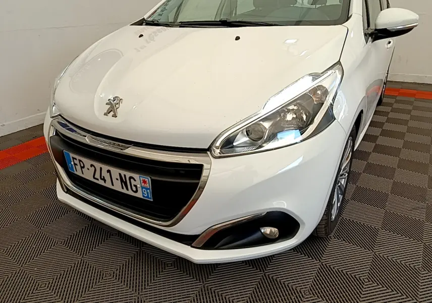 Vue 3/4 avant droite d'une Peugeot 208 blanche avec phares et calandre chromée visibles en intérieur.