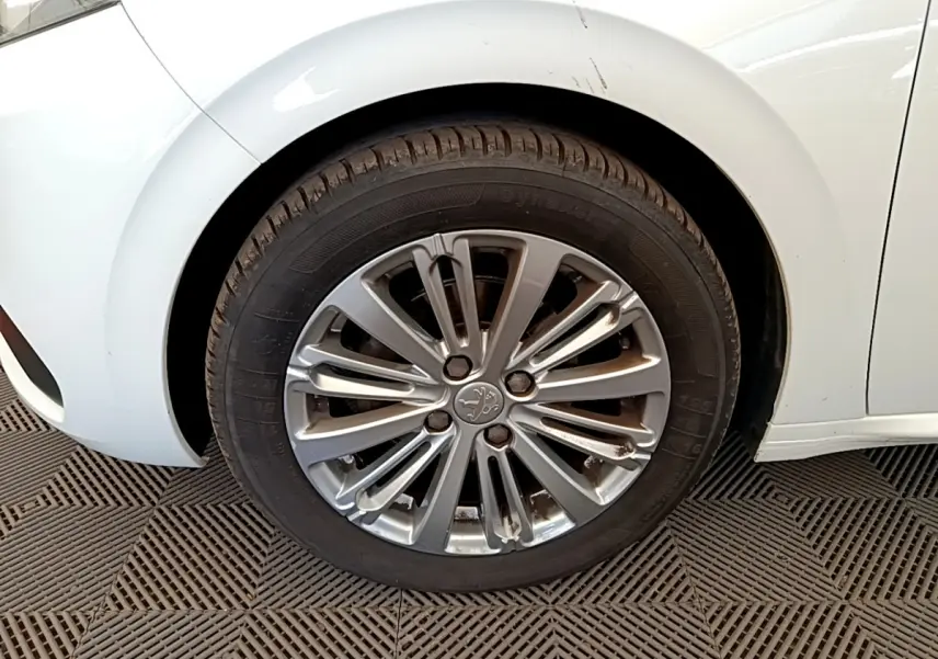 Gros plan sur la roue avant gauche de la Peugeot 208 blanche, mettant en valeur la jante alliage au design moderne.