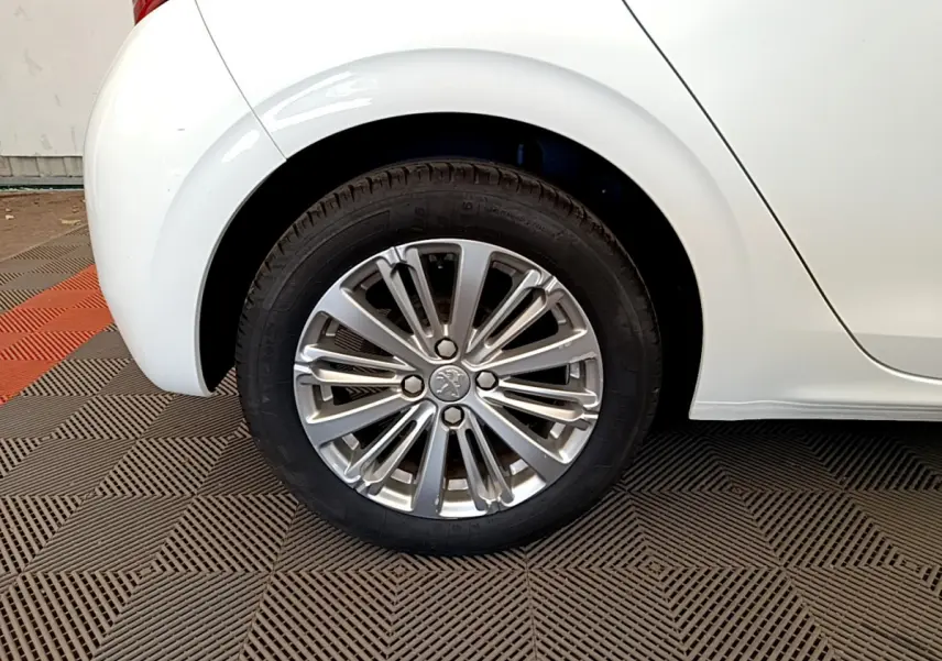 Gros plan sur la roue arrière droite d'une Peugeot 208 blanche, mettant en valeur la jante alliage au design moderne.