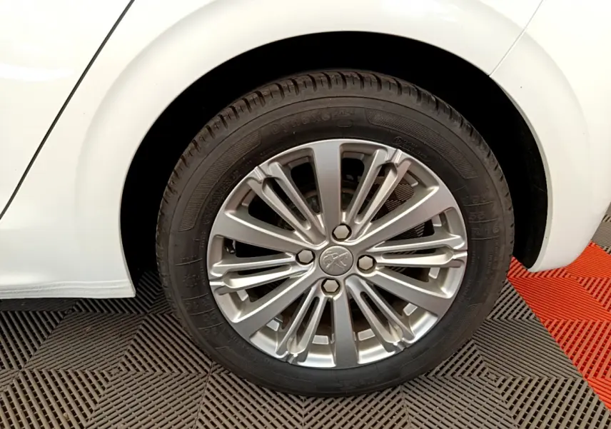 Gros plan sur la roue arrière droite d'une Peugeot 208 blanche avec jante alliage multibranches élégante.