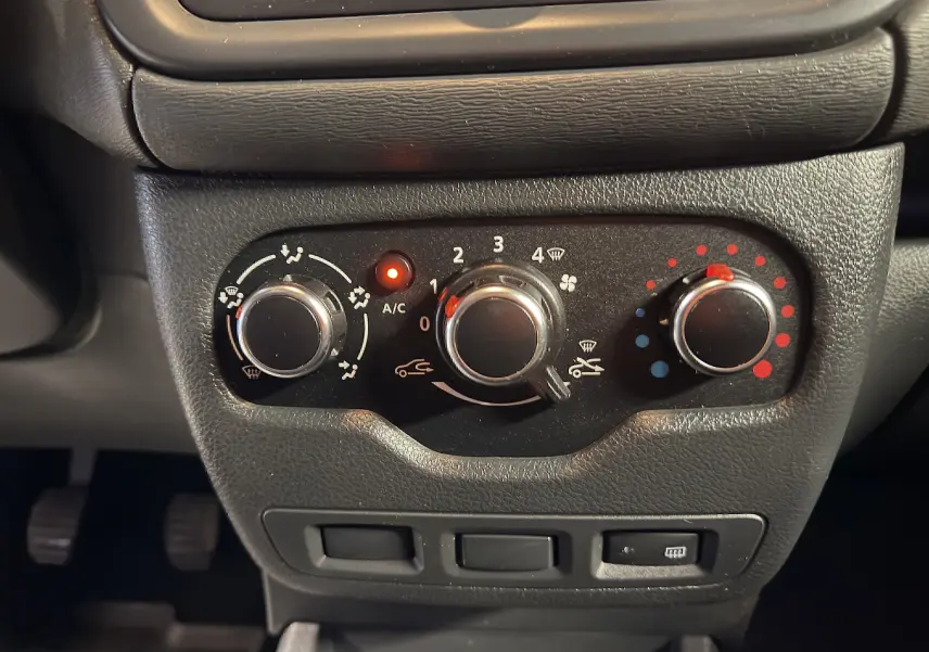 Gros plan sur les commandes de climatisation du tableau de bord d'un Dacia Dokker gris, avec voyants allumés.