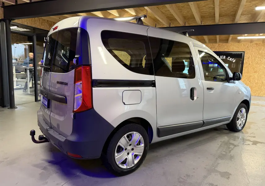 Vue 3/4 arrière droite d'un Dacia Dokker gris 2019 avec attelage et vitres teintées en intérieur showroom.