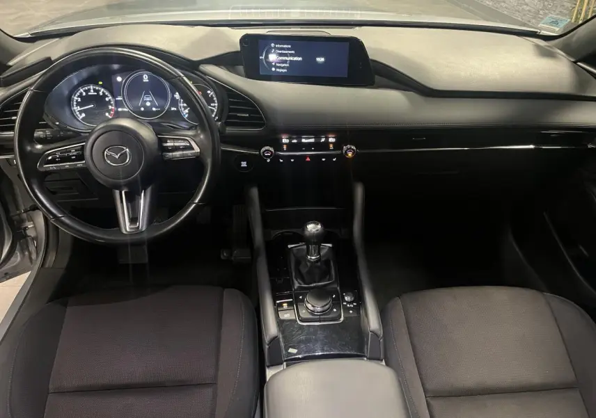 Intérieur de la Mazda3 2023 vu de face, tableau de bord noir avec écran central et volant cuir multifonctions.