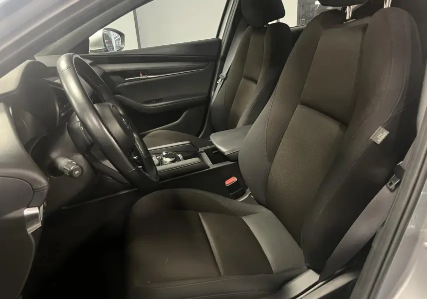Intérieur noir de la Mazda3 2023, vue côté conducteur avec sièges tissu et console centrale visible.