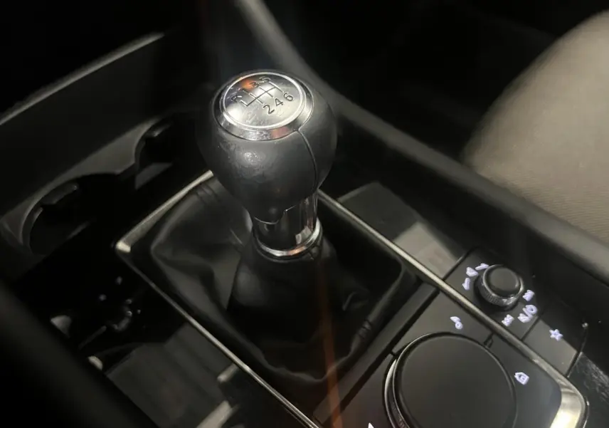 Gros plan sur le levier de vitesses manuel noir de la Mazda3 2023, entouré de commandes et porte-gobelets.