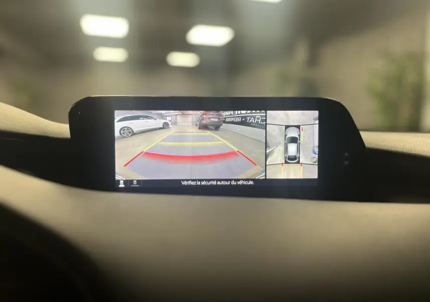 Affichage caméra 360° sur écran intérieur de Mazda3 grise, vue arrière et vue aérienne du stationnement.