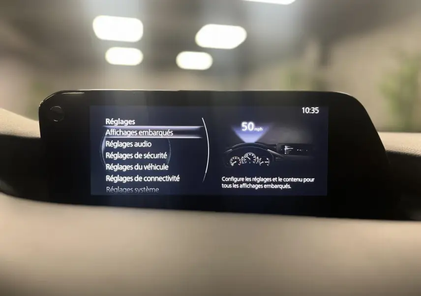 Écran central de la Mazda3 2023 affichant le menu des réglages embarqués dans un intérieur gris sobre.