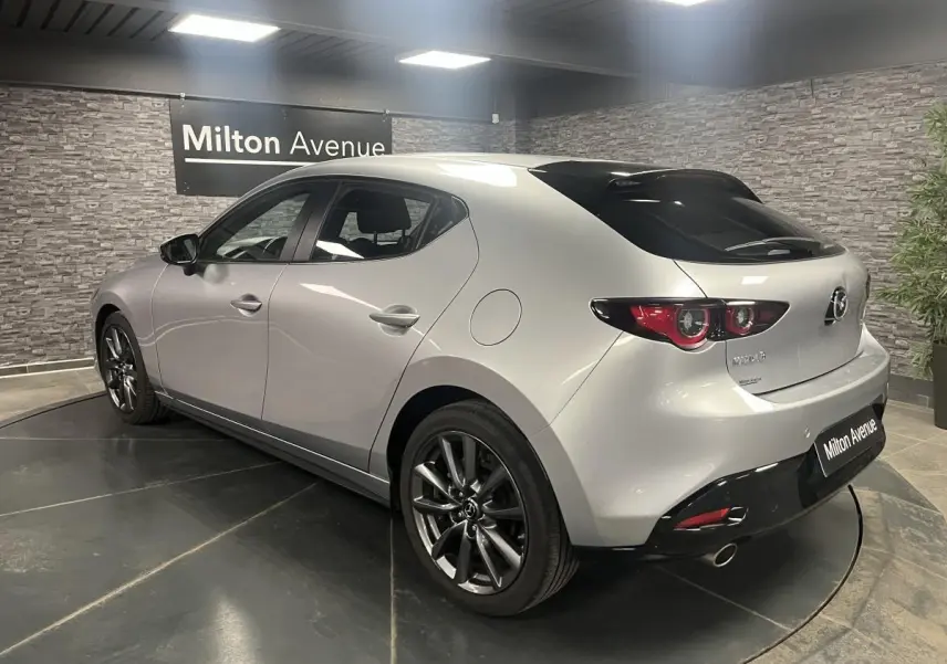 Vue 3/4 arrière droite d'une Mazda3 gris métallisé avec jantes alliage 18'' et becquet de toit noir.