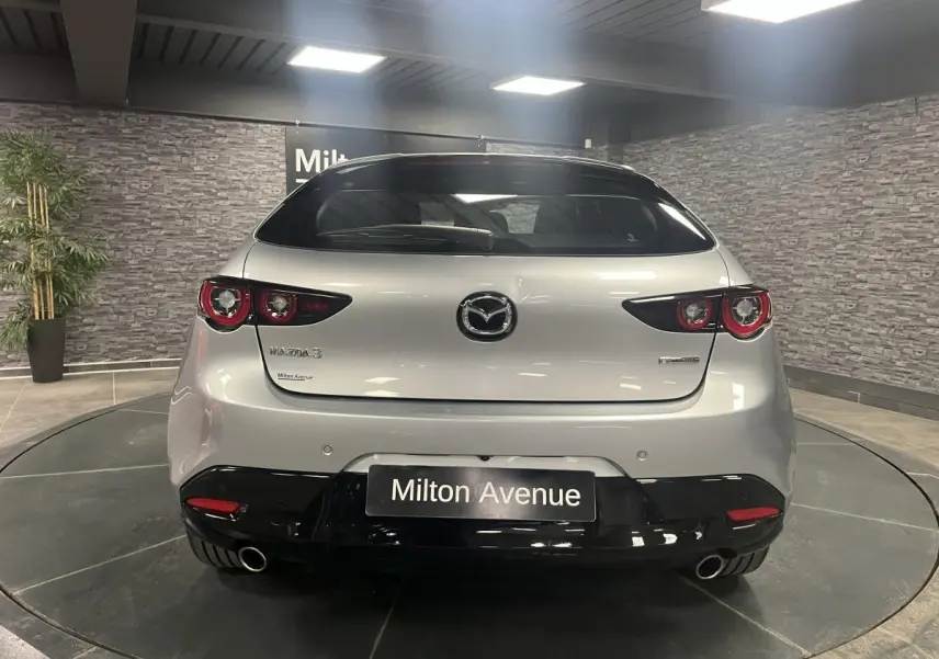 Vue arrière d'une Mazda3 gris métallisé avec double sortie d'échappement et toit noir dans un showroom.