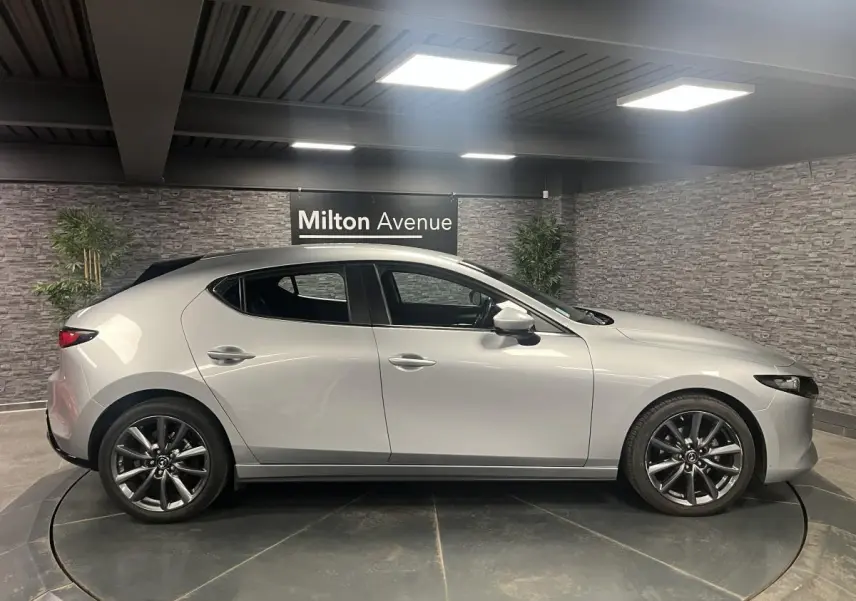Vue latérale droite d'une Mazda3 2023 gris métallisé avec jantes alliage 18 pouces dans un showroom.