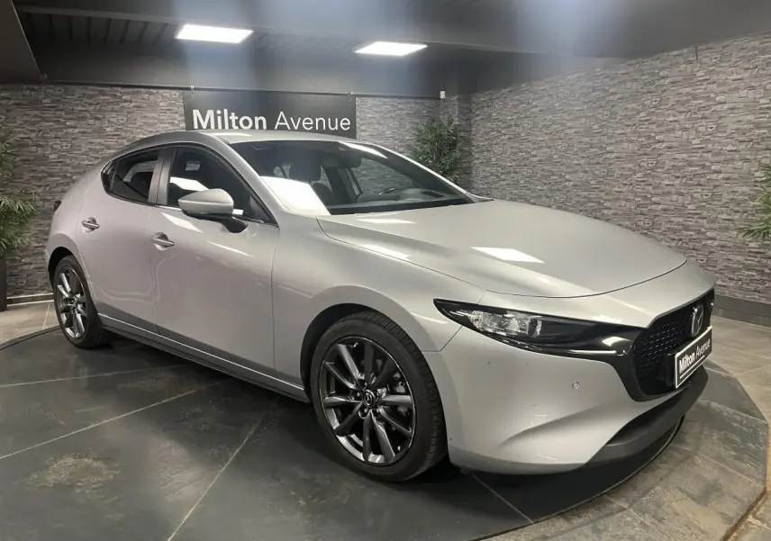 Vue 3/4 avant droite d'une Mazda3 gris métallisé avec calandre noire et jantes alliage 18 pouces grises.