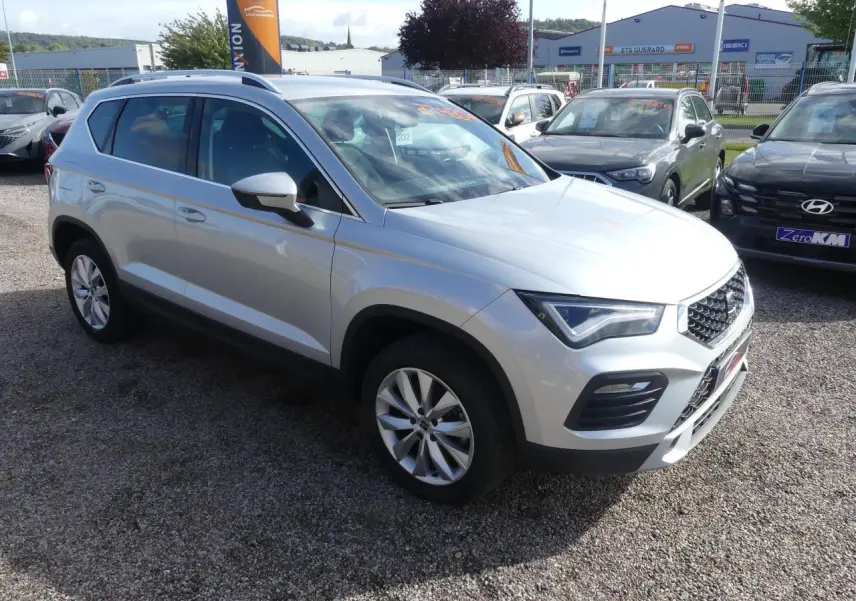 SEAT Ateca gris clair vue 3/4 avant droit, avec jantes alliage 17'' et calandre chromée sur parking extérieur.