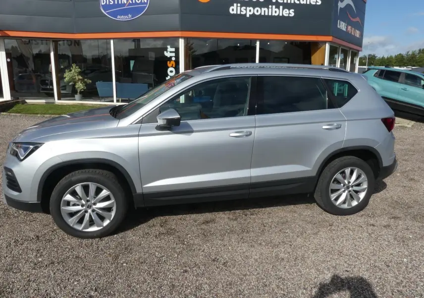 Vue de profil côté gauche d'un SUV SEAT Ateca gris clair garé devant un concessionnaire avec jantes alliage 17 pouces.