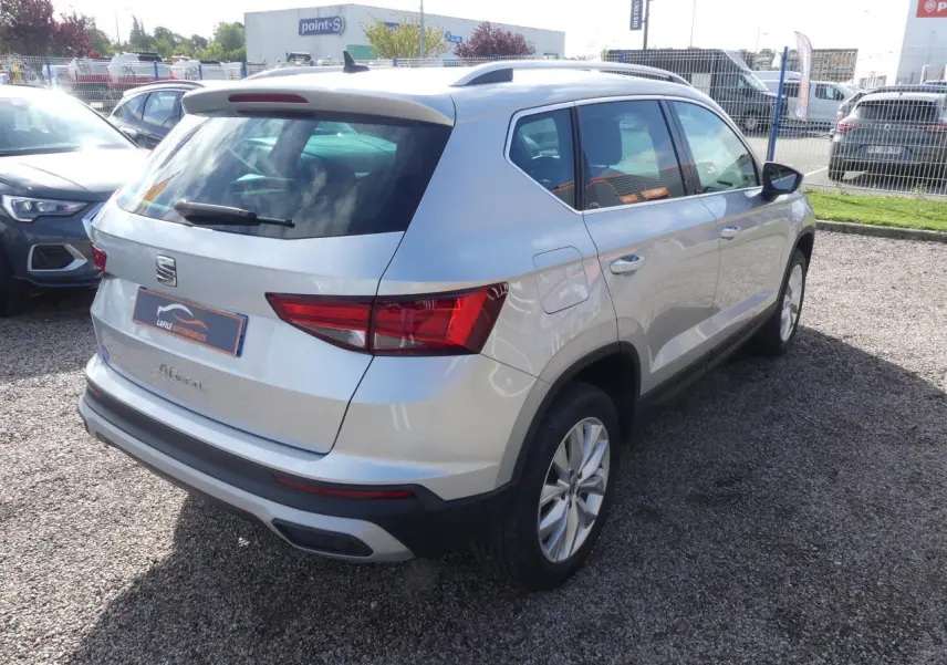 Vue 3/4 arrière droite d'un SEAT Ateca gris clair avec jantes alliage 17'' et barres de toit chromées.