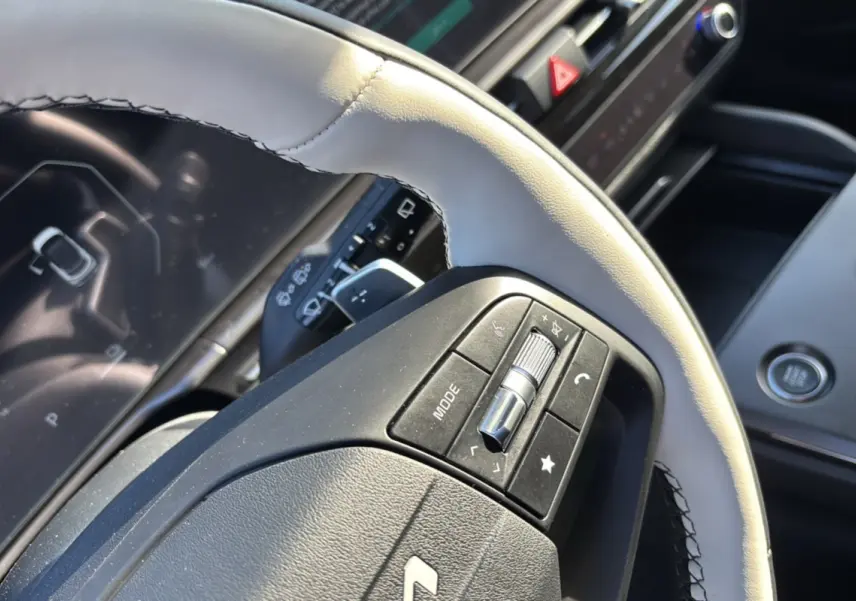 Gros plan sur le volant cuir blanc nacré avec commandes multifonctions du Kia Sportage 2026 hybride, tableau de bord en arrière-plan.