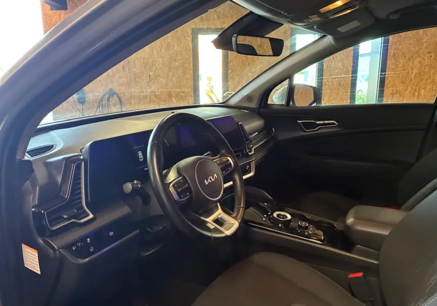 Intérieur du Kia Sportage 2024 hybride en vue côté conducteur, avec tableau de bord noir et volant multifonction.