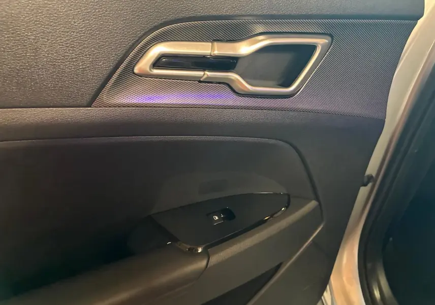Détail de la poignée intérieure et commande de vitre sur la porte avant gauche d’un Kia Sportage gris 2024.