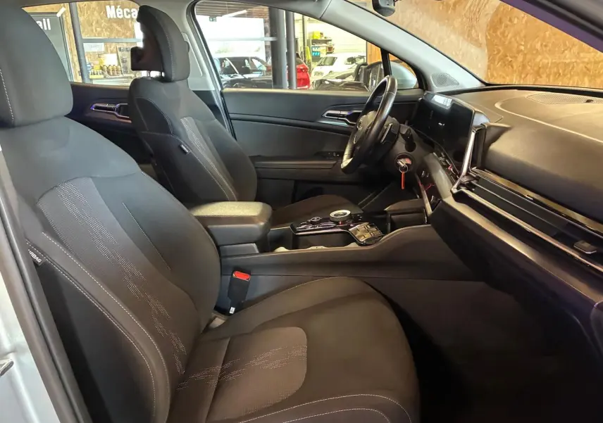 Vue intérieure côté conducteur du Kia Sportage 2024 gris, montrant sièges noirs et tableau de bord moderne avec écran tactile.