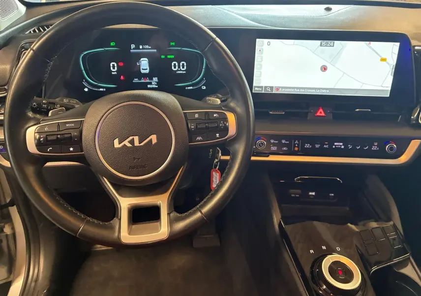 Vue intérieure du poste de conduite du Kia Sportage hybride 2024, avec volant cuir, tableau de bord numérique et écran tactile large.