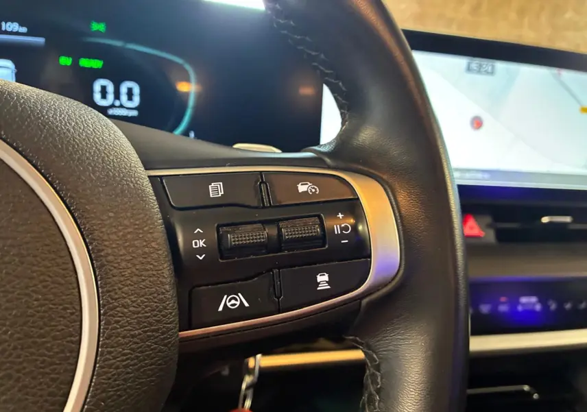 Gros plan sur le volant noir du Kia Sportage hybride 2024, avec commandes de régulateur et affichage numérique en arrière-plan.