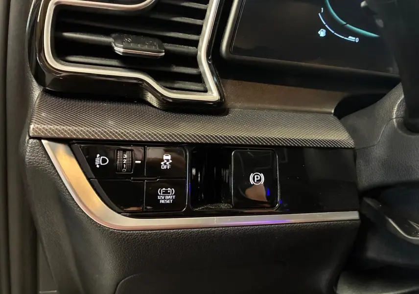 Détail du tableau de bord côté gauche du Kia Sportage gris 2024, avec commandes d'éclairage et frein à main électronique.