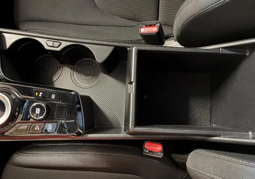Vue plongeante sur la console centrale du Kia Sportage hybride 2024, avec rangement ouvert et commandes de boîte auto.