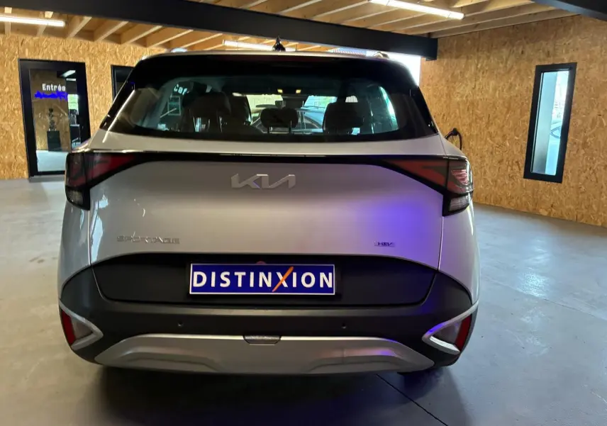 Vue arrière d’un KIA Sportage gris 2024 hybride, avec feux arrière reliés par une bande noire distinctive.