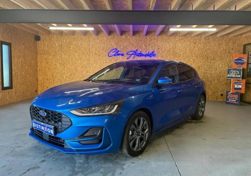 Ford Focus 1.0 EcoBoost bleu en 3/4 avant droit, avec calandre hexagonale et jantes alliage visibles.