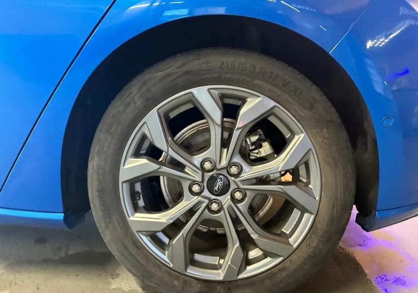 Gros plan sur la roue arrière droite d'une Ford Focus bleue 2024, mettant en valeur la jante alliage au design moderne.