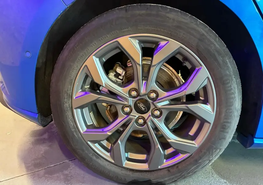 Gros plan sur la roue avant gauche d’une Ford Focus bleu 2024 avec jante alliage et logo Ford au centre.