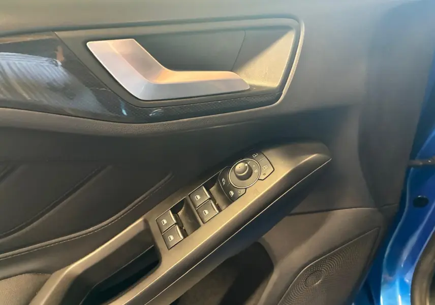 Détail de la porte avant gauche de la Ford Focus bleue 2024, avec commandes électriques des vitres et poignée argentée.