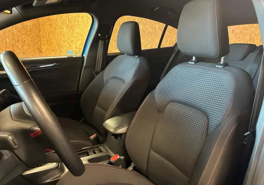 Vue intérieure côté gauche de la Ford Focus 2024 bleu, sièges avant en tissu noir avec surpiqûres rouges.