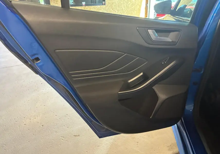 Vue rapprochée de la porte arrière gauche bleue d'une Ford Focus 2024, avec garniture intérieure noire et poignée intégrée.
