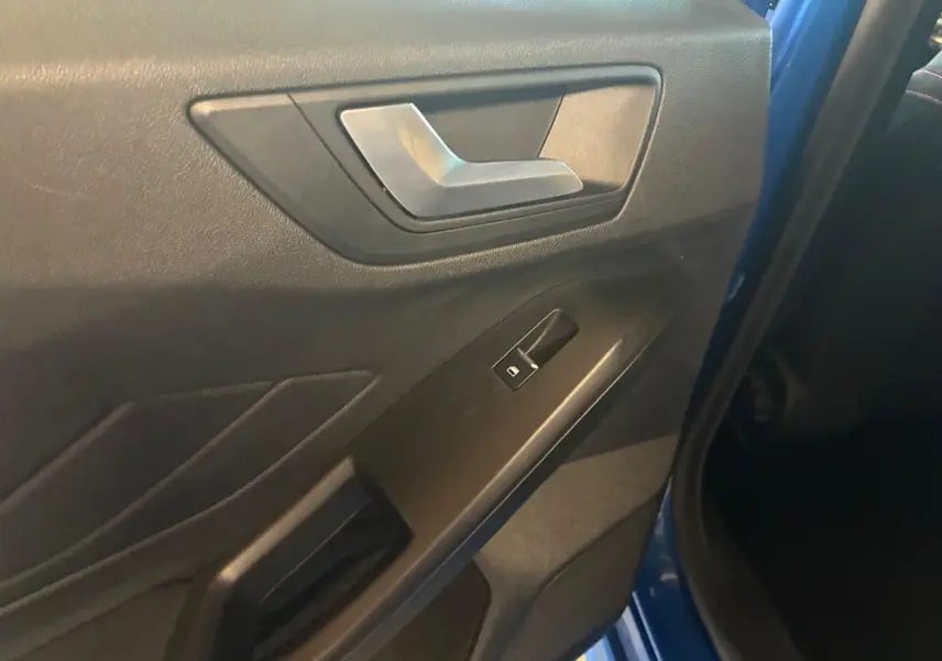 Gros plan sur la porte intérieure côté gauche d’une Ford Focus bleue 2024, avec poignée argentée et bouton de vitre électrique.