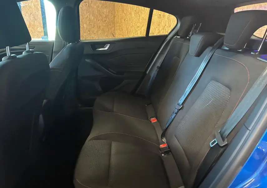 Vue intérieure arrière côté droit de la Ford Focus 2024 bleu, montrant les sièges arrière en tissu noir avec surpiqûres rouges.