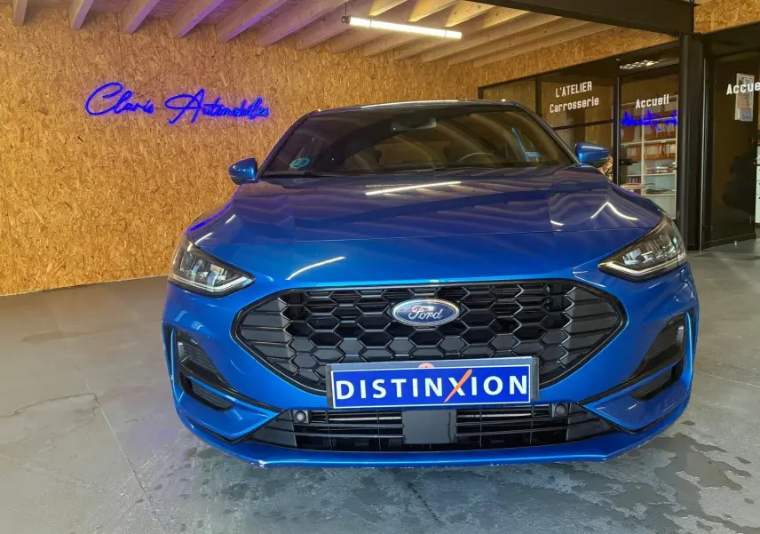 Vue frontale d'une Ford Focus 1.0 EcoBoost MHEV bleu vif, avec calandre hexagonale noire et logo Ford centré.