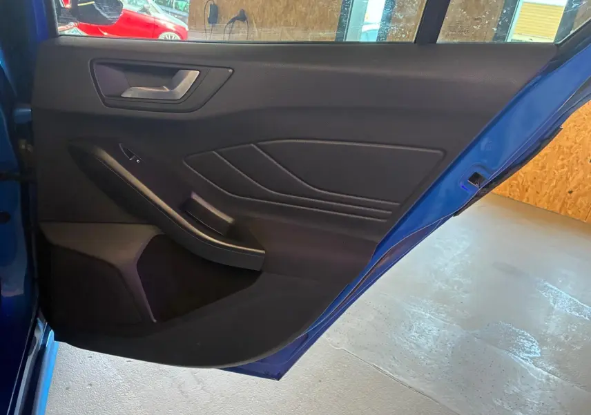 Vue intérieure de la porte arrière droite bleu foncé d’une Ford Focus 2024 avec garniture noire et poignée argentée.