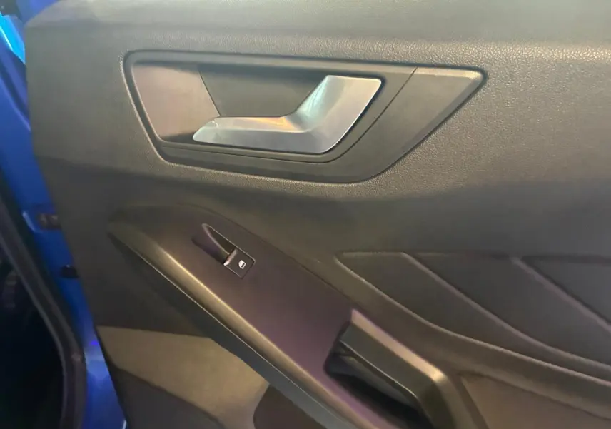 Détail de la porte intérieure côté gauche d’une Ford Focus 2024 bleue, avec poignée argentée et commande de vitre.