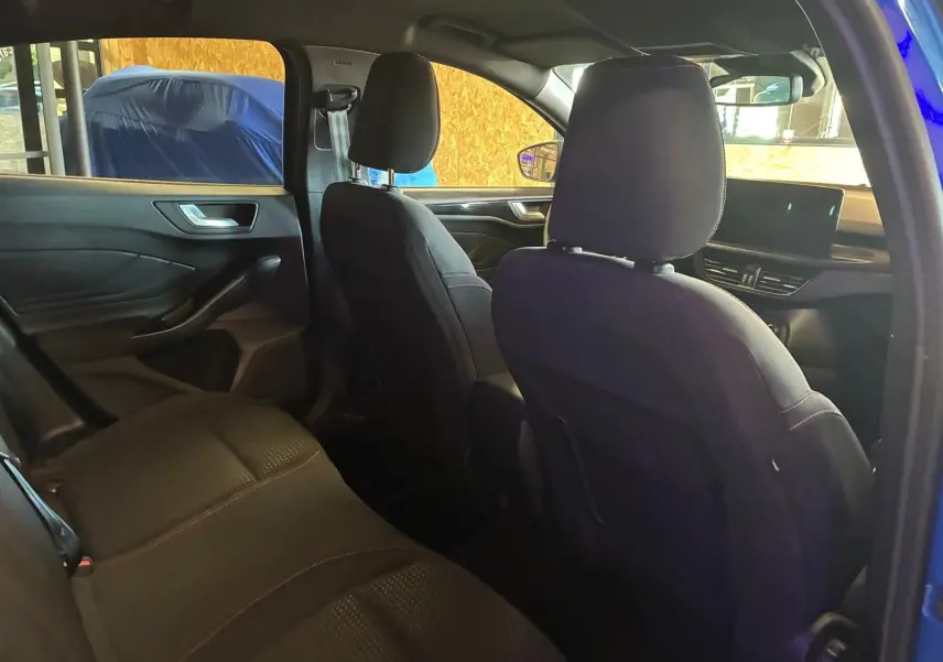 Vue intérieure arrière côté gauche de la Ford Focus 2024 bleu, sièges tissu noir avec surpiqûres rouges et tableau de bord visible.